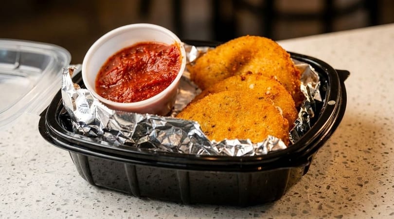 Fried mozzarella cheese with marinara sauce in a black takeout container lined with foil.